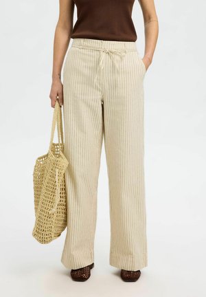 Crème-kleurige wijde broek met verticale strepen, met een verstelbare taille en zijzakken. Vergezeld door een geweven beige tote bag.