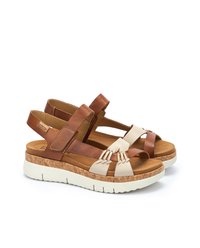 Sandali in pelle marrone con accenti crema, cinturini regolabili, suola simile al sughero e base in gomma bianca. Presentano un design intrecciato sulla parte anteriore.
