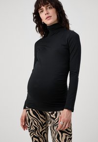 Fekete, hosszú ujjú kismama blúz magas nyakkivágással, bézs és fekete zebra mintás, slim fit leggings-szel párosítva.