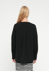 Chemise noire à manches longues avec une coupe décontractée, dotée d'une couture de yoke au dos et de boutons aux poignets, associée à une jupe rayée.