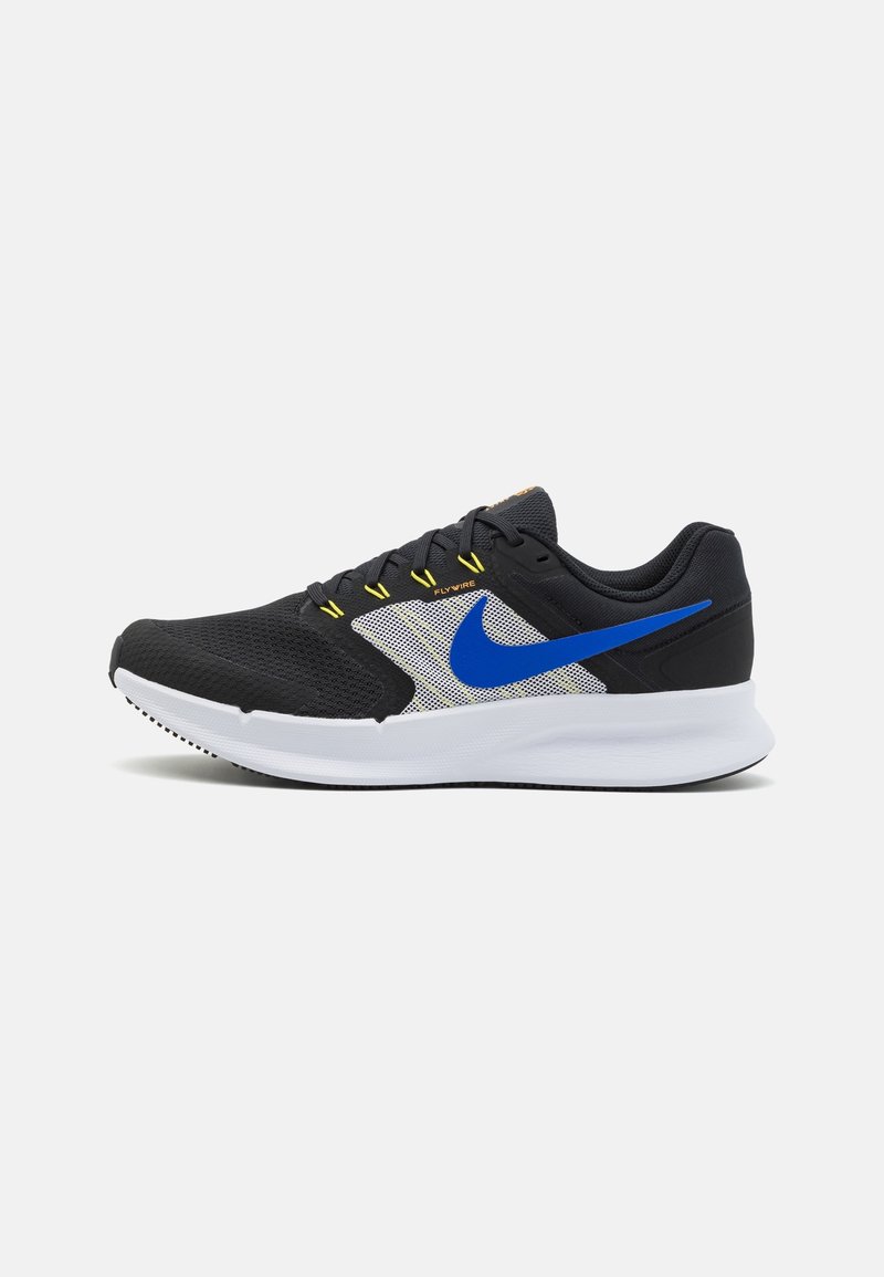 Chaussure de course noire et blanche avec le logo Nike bleu, boucles de lacets jaunes et semelle blanche sur un fond clair uni.