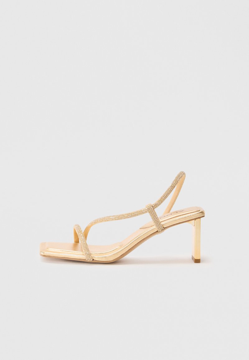 Strappy high-heeled sandal in gold, featuring embellished straps, a square toe design, and a thin block heel for stability.
