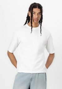 Hvid bomulds T-shirt med rund hals og korte ærmer, der har en afslappet pasform og et minimalistisk design. Bæret med lyseblå denim.