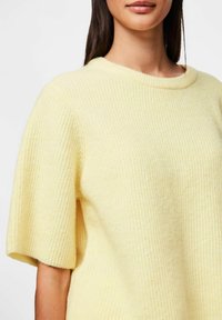 Krótki rękaw żółty sweter wykonany z teksturowanej tkaniny z prążkowanym wzorem i szerokim, okrągłym dekoltem.
