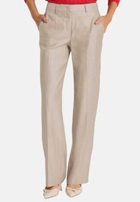 Beige broek met een getailleerde pasvorm, wijde benen, scherpe zakken en subtiele plooien. Gemaakt van een gladde stof. Gecombineerd met lichter gekleurde schoenen.