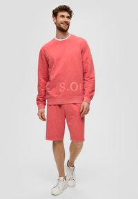 Ensemble de sweatshirt et de shorts rose clair en tissu doux, avec un col rond, des poignets côtelés et un logo imprimé sur le devant.