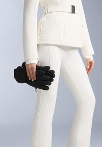 Svarta isolerade handskar med vadderad design och femfingerskonstruktion, hållna avslappnat i en hand, kombinerade med en figursydd vit outfit.