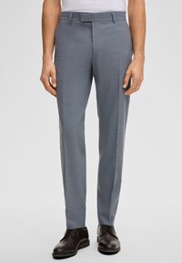 Lichtgrijze op maat gemaakte broek met een gestructureerd patroon, twee zijzakken en een platte voorkant, gecombineerd met donkerbruine schoenen.