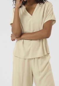 Top beige a V con maniche corte, texture liscia, design a strati. Abbinato a pantaloni a gamba larga con tasche grandi.