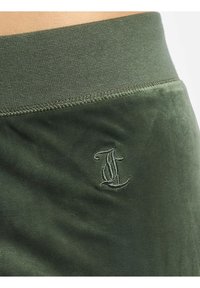 Gröna sammetsshorts med ribbad midja, som har en subtil broderad logotyp på vänster sida. Slät textur och åtsittande design.