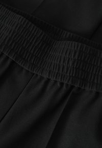 Tissu noir avec une large ceinture élastique froncée montrant des coutures texturées et un matériau lisse en dessous.