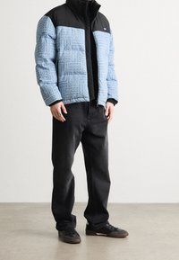 Kurtka pikowana z czarną górną częścią i niebieską, wzorzystą dolną częścią z powtarzającym się napisem "HUGO". Czarne dżinsy i ciemne buty.