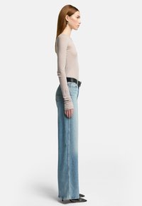Lys beige langærmet top parret med højtsiddende lyseblå straight-leg jeans, med diskrete syninger, komplementeret af sorte spidse sko.