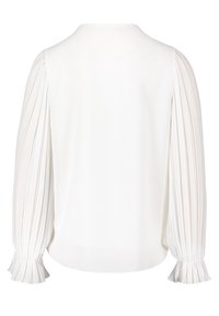 Blouse blanche à manches longues plissées avec poignets à volants, vue de dos sur un fond blanc uni.