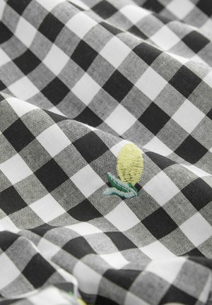 Zwart-wit geblokte stof met een gladde textuur, met een geborduurd geel ananasontwerp met groene accenten.