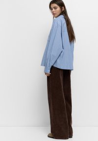 Camicia oversize a righe blu e bianche con maniche lunghe, abbinata a pantaloni a gamba larga in velluto a coste marrone. Tessuto morbido e vestibilità comoda.