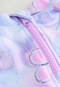 Violeta zip-up jaka ar tauriņu rakstu. Satur mirdzošas akcentus un mīkstu auduma tekstūru. Iekļauj lavandas krāsas rāvējslēdzēju un kapuci.