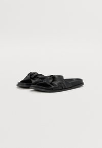 Black slip-on sandals featuring a knotted design in soft leather, flat sole, and smooth texture, suitable for casual wear.