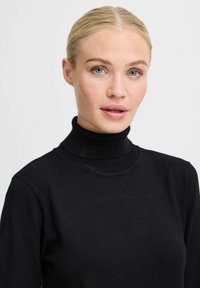 Pull à col roulé noir avec un design ajusté, un col côtelé et une texture douce, affichant une silhouette simple et classique.