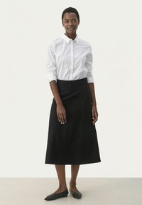 Camicia bianca con maniche lunghe, abbinata a una gonna nera midi. L'outfit presenta una vestibilità su misura e texture morbide, completato da scarpe nere basse.