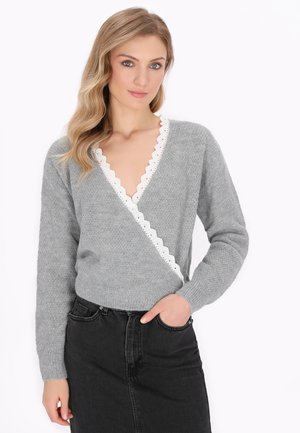 Grijze gebreide trui met een diepe V-hals en een witte geschulpte kanten rand. In combinatie met een zwarte denim rok.