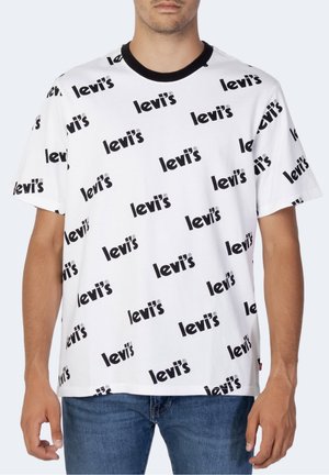 Homme portant un T-shirt blanc avec des logos "Levi's" noirs répétitifs et un col noir, associé à un jean bleu.
