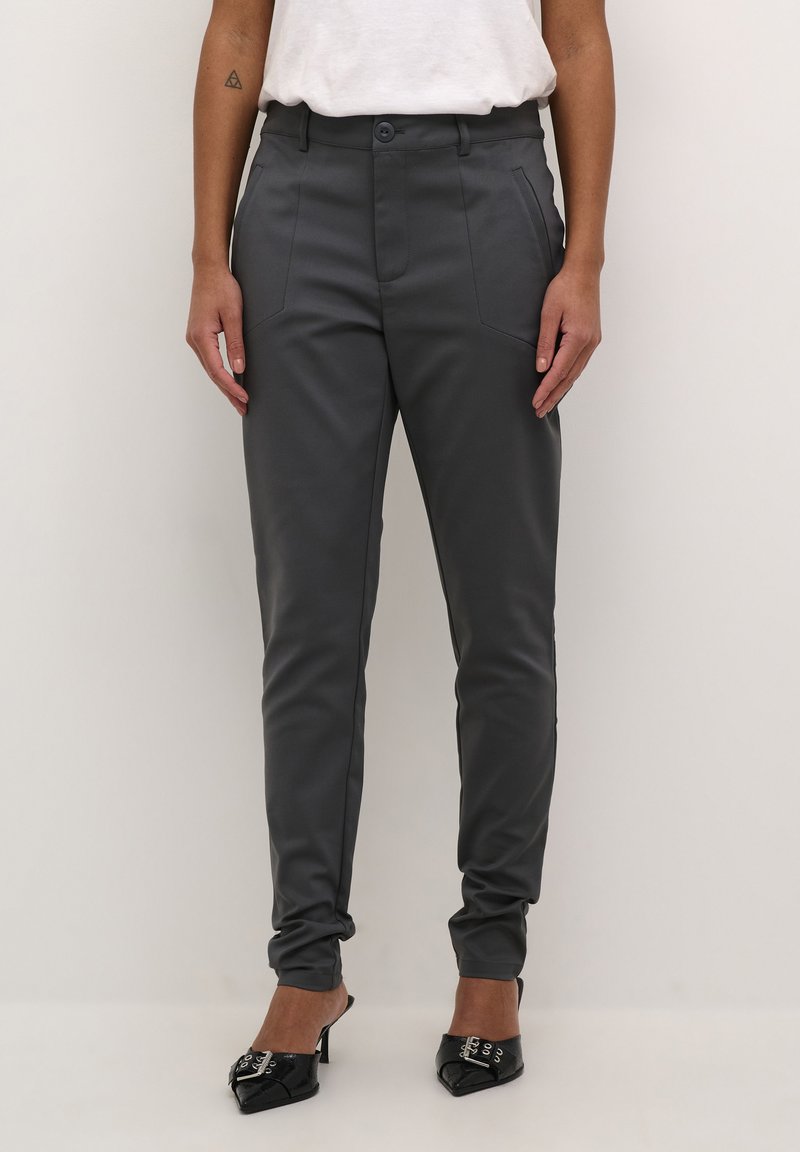 Pantalons gris cintrés avec une texture lisse, des poches avant et un design ajusté. Associés à des chaussures noires à talons aiguilles.