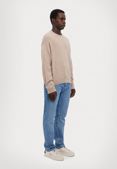 Jersey de manga larga beige, jeans de mezclilla claros y zapatillas blancas con detalles en negro. Textura lisa, sin patrones o logotipos visibles.