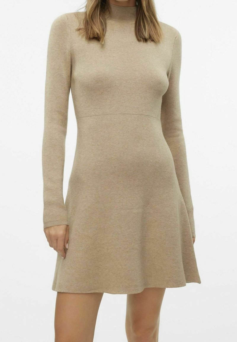 Abito a maglia beige con maniche lunghe, corpino aderente e gonna svasata indossato da una persona su uno sfondo bianco uniforme.