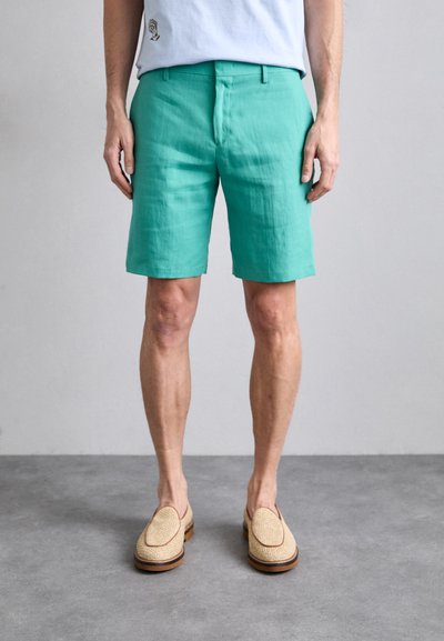 Pantaloni scurți din in turcoaz cu un front plat, buzunare laterale și o talie medie, asortați cu pantofi slip-on din fibră de iută bej.