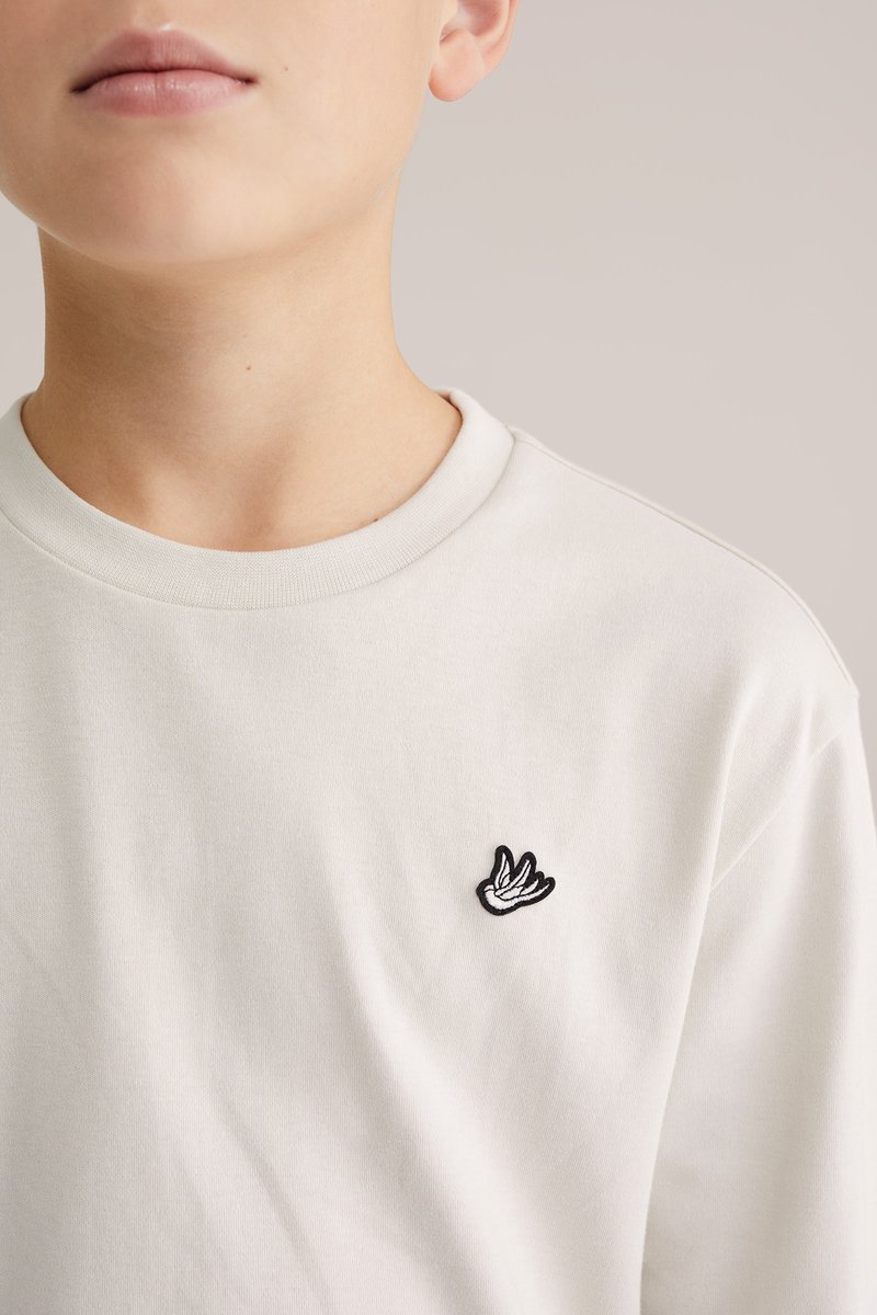 Világosszürke pamutpóló környakkal és egy kis fekete, hímzett mintával a bal mellrészen. Puha, sima tapintású anyag.