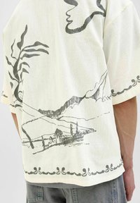 Chemise à manches courtes en crème clair avec un tissu texturé, ornée d'un imprimé paysager gris de montagnes et de bâtiments au niveau de l'ourlet.