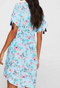 Vestido floral de tela azul clara con flores rosas y moradas. Mangas cortas con detalles de lazo y borlas, corte relajado, a la altura de la rodilla.