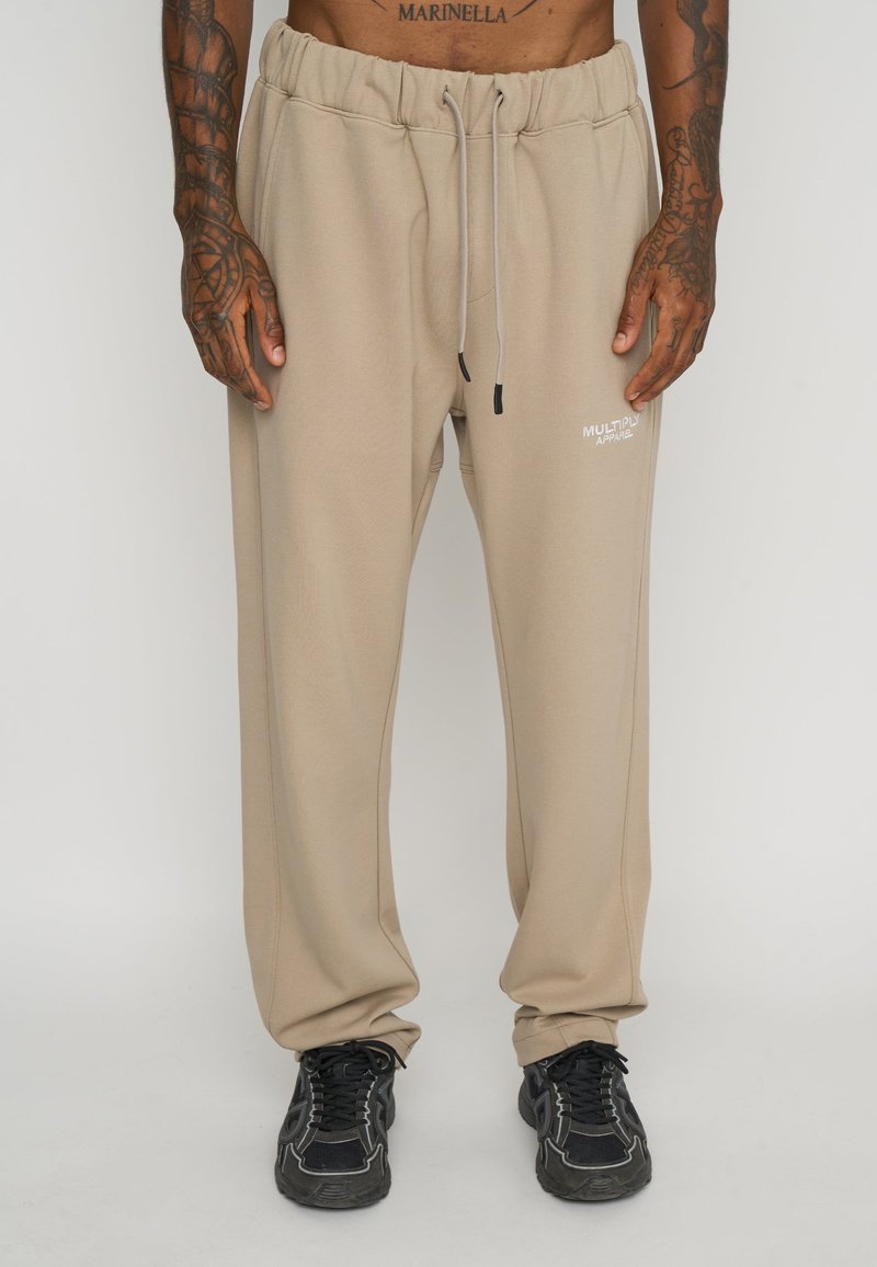 Beige sweatpants with an elastic waistband and drawstring. Side pockets and a small white logo on the thigh. Textured, soft fabric.
