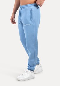 Jasnoniebieskie dresy z elastycznym pasem, bocznymi kieszeniami i białym logo. Połączone z białymi trampkami o teksturowanej podeszwie.