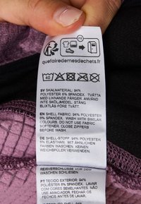 Étiquette d'entretien indiquant la composition du tissu : 94 % polyester, 6 % spandex. Instructions multilingues pour le lavage et l'entretien. Tissu texturé.