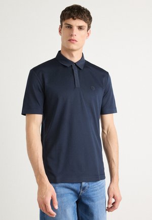 Tricou polo bleumarin dintr-un material neted, cu guler și deschidere cu nasturi. Prezintă un mic logo embosat pe piept. Mâneci scurte.