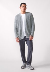 Ljusgrå stickad cardigan med öppen fram, fickor och långa ärmar, bärs över en vit t-shirt och matchas med mörkgrå byxor.