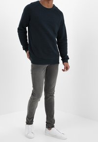 Sudadera azul oscuro con cuello redondo y mangas raglán, combinada con jeans ajustados grises y zapatillas blancas. Textura de tela suave.