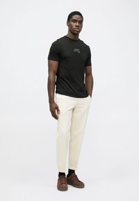 Tricou negru cu mânecă scurtă, cu un logo discret, asortat cu pantaloni crem cu croi conic și adidași maronii. Design simplu, potrivire casuală.