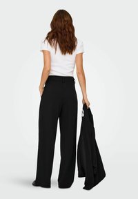 Pantaloni larghi neri realizzati in tessuto morbido, a vita alta, con tasche e passanti per cintura; abbinati a una t-shirt bianca aderente e a una giacca nera.