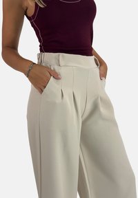 Pantalon beige à jambes larges avec plis et poches latérales, confectionné dans un tissu lisse, associé à un débardeur ajusté couleur bordeaux.