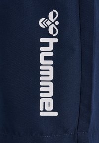 Granatowy materiał z białym logo "hummel" i stylizowanym symbolem trzmiela nadrukowanym pionowo.