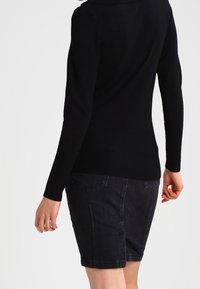 Pull noir côtelé avec un col montant, associé à une jupe en denim foncé. L'ensemble comprend des manches longues et une silhouette ajustée.