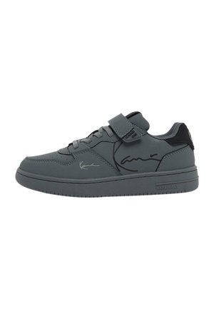 Graue Sneaker mit Synthetik-Obermaterial, Schnürung und Klettverschluss, Gummisohle und Logo-Akzenten an der Seite und Zunge. Schlichtes Design, glatte Textur.
