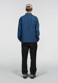 Giubbotto di jeans blu scuro, vestibilità comoda, con maniche lunghe e colletto. Abbinato a pantaloni neri e calzature grigie. Sfondo neutro.