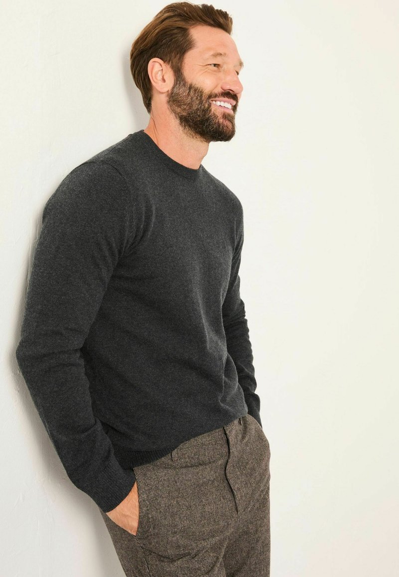 Dunkelgrauer Strickpullover mit rundem Halsausschnitt, taillierten Ärmeln und gerippten Bündchen, kombiniert mit strukturierten braunen Hosen.