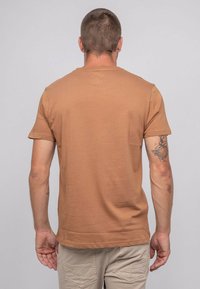 T-shirt à manches courtes marron en coton, avec un col ras du cou et une texture lisse. Design minimaliste sans motifs ni accents visibles.