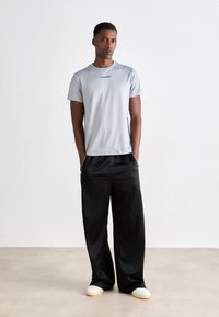 Tricou scurt de culoare gri deschis cu mâneci scurte, cu logo-ul albastru "Calvin Klein", asortat cu pantaloni negri lejerați și încălțăminte albă. Design minimalist și croială.
