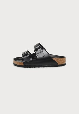 Sandale noire Birkenstock avec deux brides réglables et semelle en liège sur fond blanc plat.